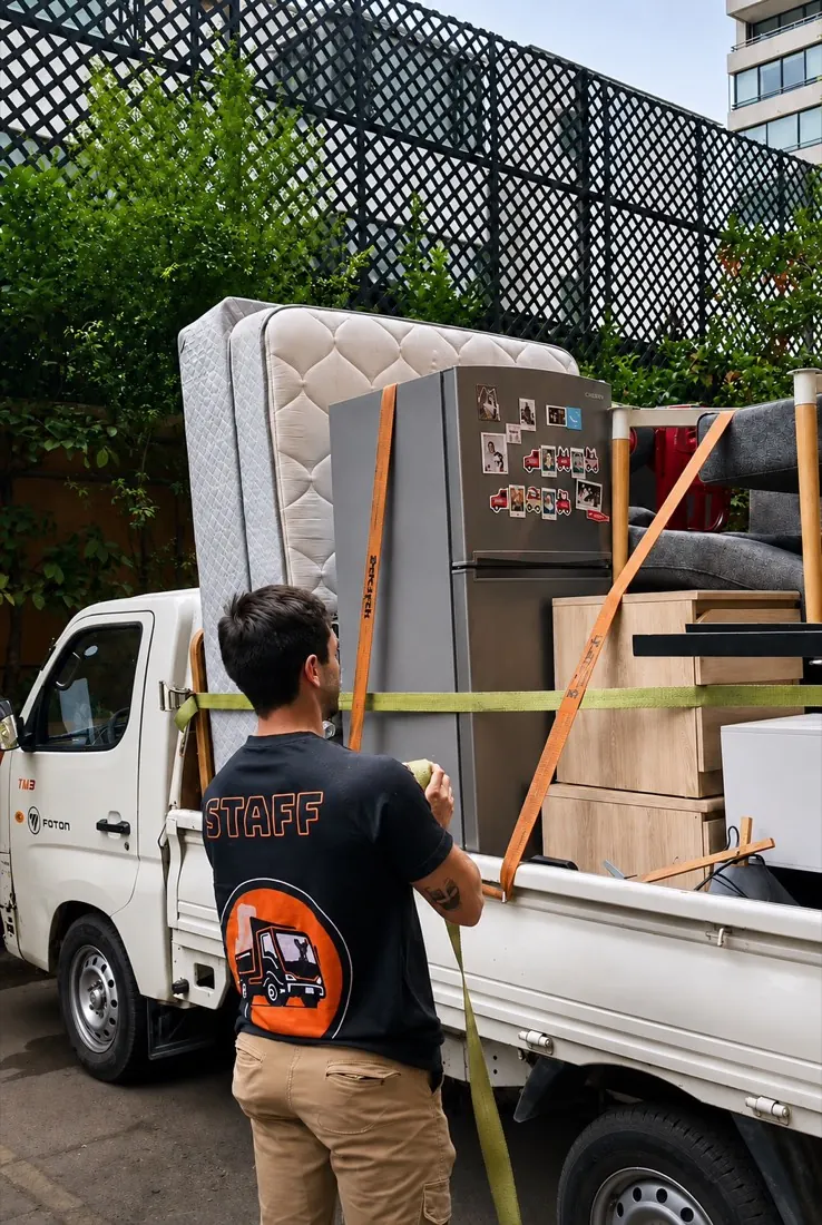 Trabajador de Yoru Express asegurando un colchón y un refrigerador con correas en un camión